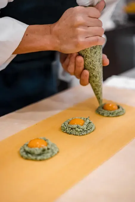 A chef piping herb mousse onto a wooden board